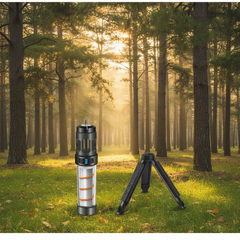 Black tripod and cylindrical device on a wooden surface with blurred lights and plants in the background